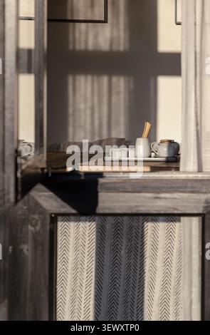 Chongqing, China - 9 Jun 2026 - intimate glimpse through an open wooden window reveals a serene tea set resting on a sun-dappled table, enveloped in s Stock Photo