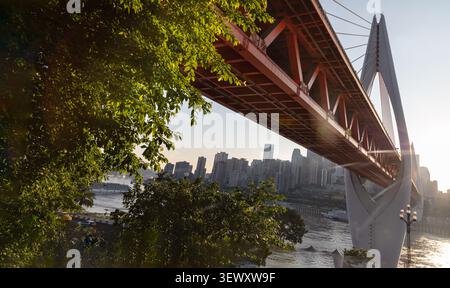 a dramatic low angle of the iconic Qiansimen Bridge cuts a powerful diagonal across the frame, showcasing its striking orange-red steel truss structur Stock Photo