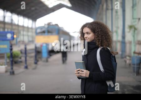 Thoughtful woman holding a book on a train platform Stock Photo
