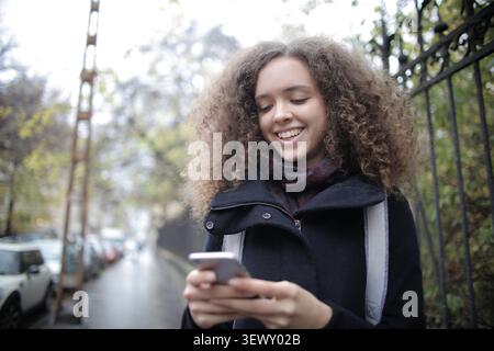 Happy curly haired woman using her smartphone outside Stock Photo