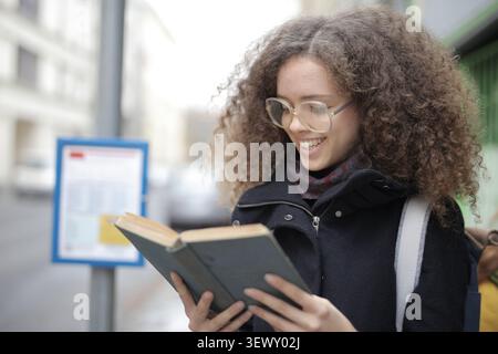 Young woman with curly hair reads a book outside Stock Photo