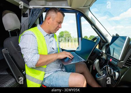Side view of a professional delivery man typing on laptop computer inside his commercial van Stock Photo