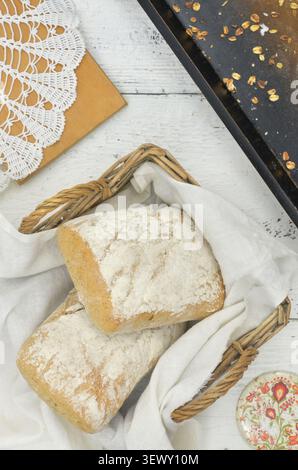 Local ingredients, regional, local taste: Bread rolls arranged on linen cloth in wicker basket. Brown tray, spilled oat flakes and cutting board. Stock Photo