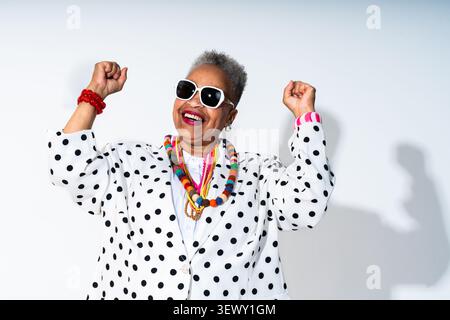 Black senior woman wearing modern clothing portrait on background - senior woman wearing a polka dot blazer and colorful jewelry, joyfully expressing Stock Photo