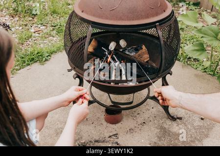 Father and daughter roast marshmallows over a backyard fire pit Stock Photo