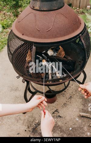 Hands roasting marshmallows over an outdoor fire pit Stock Photo