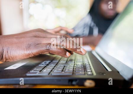 close up of hands of young african woman sitting at desk in office working and typing on laptop, enterpreneurship in africa Stock Photo