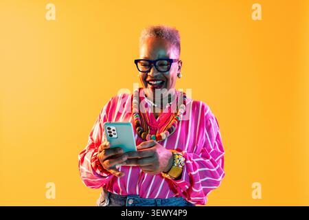 Black senior woman wearing modern clothing portrait on background - happy senior african american woman communicating digitally Stock Photo