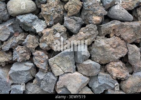 A detailed close-up shot of a textured stone wall built from rough, dark grey and brown volcanic lava rocks in Agaete. Stock Photo