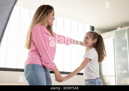 Smiling mother and daughter holding hands at home in a bright living room Stock Photo