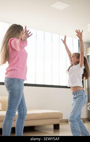 Happy mother and daughter playing together with raised arms at home Stock Photo