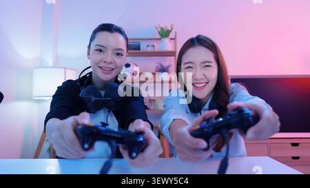 Two cheerful young Asian women playing video games with controllers at home Stock Photo