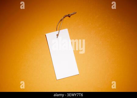 Close-up of a blank cardboard clothing tag on an orange surface. Tag used to indicate the price in retail. Stock Photo
