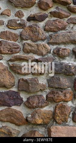 Close up of a rock and mortar wall surface with brown porous uneven stones, wide cracked mortar joints, one flat elongated stone Stock Photo