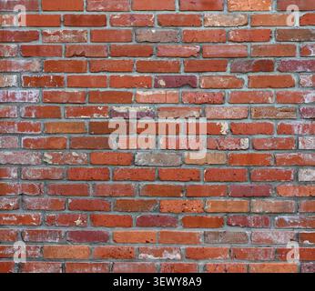 Horizontal close up of a reclaimed red brick and mortar wall surface with worn chipped cracked bricks, porous uneven mortar Stock Photo