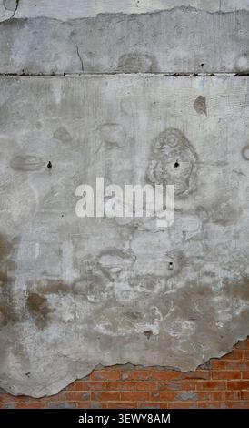 Vertical close up of a weathered decaying multilayer wall surface with concrete, water spots, and exposed red brick Stock Photo