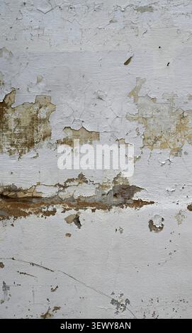 Vertical close up of an aging painted white wall surface with cracked chipped flaking paint, exposed concrete Stock Photo