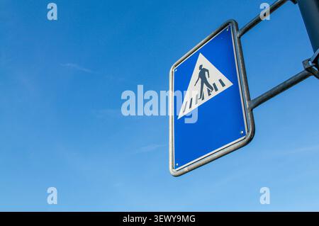 Low angle close up of a blue pedestrian crosswalk traffic sign in Switzerland. Minimalist urban street design against a clear blue summer sky backgrou Stock Photo