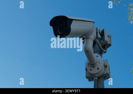 Low angle close up view of an outdoor surveillance security camera fixed on a metal post. Modern CCTV monitoring system under a clear blue summer sky Stock Photo