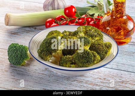 Healthy meal preparation still life. Cooked green broccoli in white bowl surrounded by fresh ingredients like cherry tomatoes, leek, and garlic. Rusti Stock Photo
