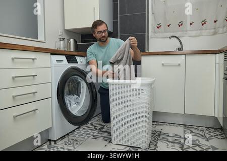 Man doing laundry at home in modern kitchen. Person loading washing machine and pouring detergent. Concept of household chores, domestic life, and hom Stock Photo