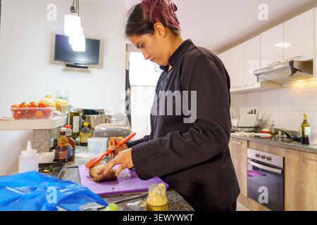 Professional female chef cooking meat in a modern kitchen, applying seasoning with a brush Stock Photo