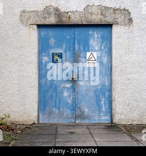 Weathered blue double doors with a 'Danger Compressed Air' sign and a 'West Lakes Sub Aqua Club' emblem. Stock Photo