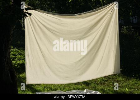 A large piece of cloth is stretched and hanging between two trees in a yard. The sun is shining, and the grass is green beneath. There are no people p Stock Photo