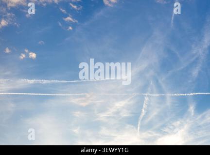 Bright blue sky covered with wispy cirrus clouds and long white airplane contrails stretching horizontally on a pleasant day in Croatia. Stock Photo