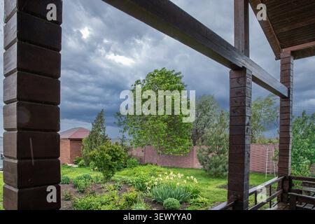 Dark storm clouds approaching over landscaped backyard viewed from wooden terrace before heavy rain Stock Photo