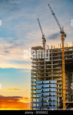 Towering construction site under vibrant sunset sky. Two cranes lift steel beams high into air Stock Photo