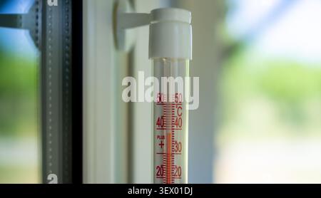 A thermometer displaying temperature outside near a window with a neutral mood and a close-up vertical perspective, featuring glass and plastic materials and white, red, green, and blue. Stock Photo