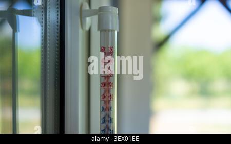 A stationary indoor thermometer positioned near a window, featuring a clear glass and plastic construction. The neutral setting and close-up view make it home decor and weather-mo. Stock Photo
