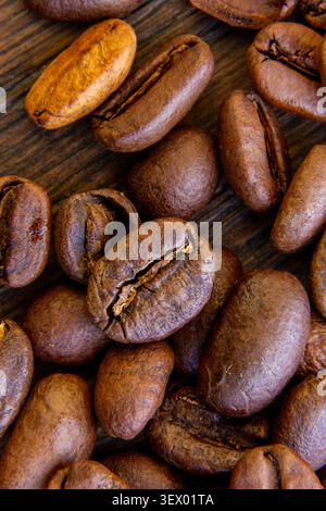 Close-up macro photograph of roasted coffee beans arranged on a rustic wooden surface. The image highlights the rich texture, natural color variations Stock Photo