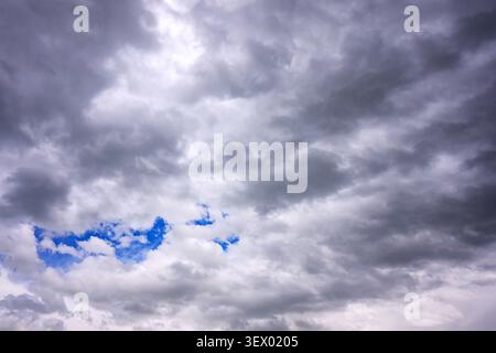Dark storm clouds cover sky. Small blue patches show through cloud cover. Sky looks heavy and overcast. Nature scene shows dramatic weather conditions Stock Photo