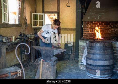 Female Blacksmith Working at Anvil in Traditional Forge Workshop With Fire and Tools Stock Photo