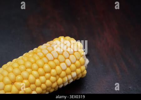 Macro view of chilled yellow maize coated in fine frost on a dark wooden surface. A refreshing snack idea with generous copy space for food design. Stock Photo
