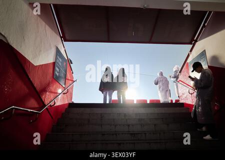 Silhouette of baseball fans at a stadium tunnel exit during a rain delay wearing ponchos and observing the field in bright lighting. Stock Photo
