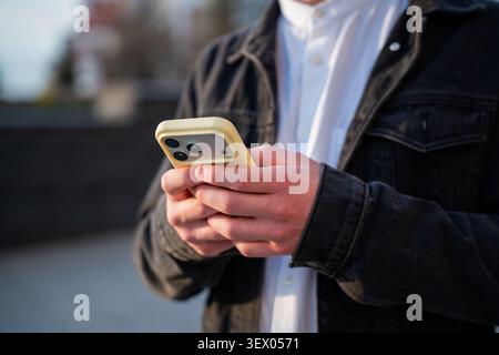 Close up of a young man using a smartphone outdoors near a modern office building during the workday. Mobile communication and digital business connec Stock Photo