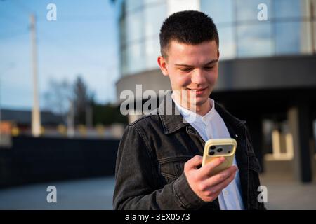 Young man using a smartphone outside a modern office building during the workday. Mobile communication and digital business connectivity. Stock Photo