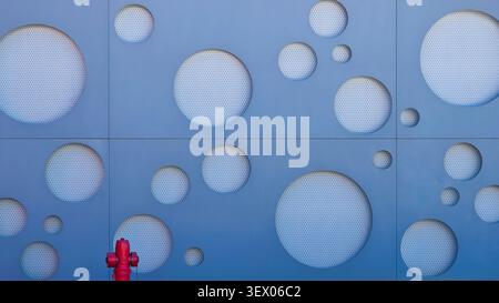 Blue modern facade with circular perforated patterns and a red fire hydrant. Stock Photo