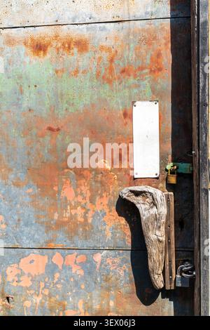 Old rust covered metal door with a shaped piece of old wood serving as a door handle. Two padlocks locking the door. Stock Photo