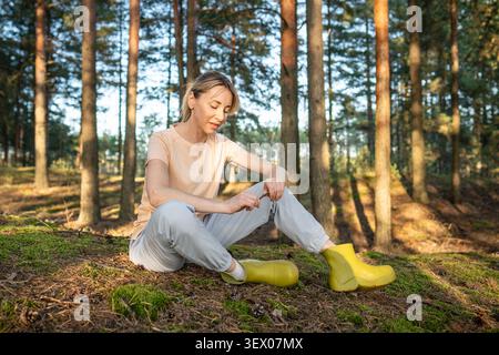 Happy relaxed woman sitting on forest ground enjoying peaceful getaway and quiet in summer woods. Stock Photo
