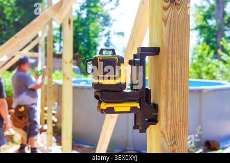Frame workers are building structure near pool using laser level for accuracy in backyard. Stock Photo