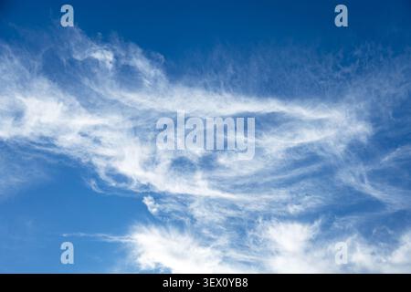 wispy cirrus clouds drifts across a vivrant blue sky on a clear day Stock Photo