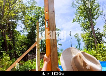 Frame worker works on erecting wooden post while using level tool under construction location Stock Photo