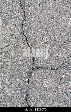 Close-up view of cracked asphalt surface with visible fissures on a paved road texture. Stock Photo