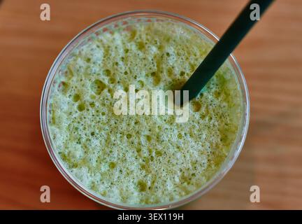 Green iced matcha smoothie served in a clear cup with a green straw, showing bubbles on the surface, resting on a wooden table Stock Photo
