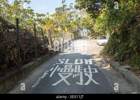 Sign on the road reads "slow" in English and Chinese, bilingual road marking on Brick Hill, standard in Hong Kong Stock Photo
