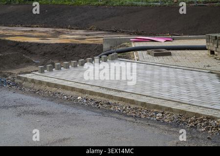 Workers set paving stones on a construction site. The area has partially finished walkways. Tools and materials are nearby. The weather looks clear wi Stock Photo